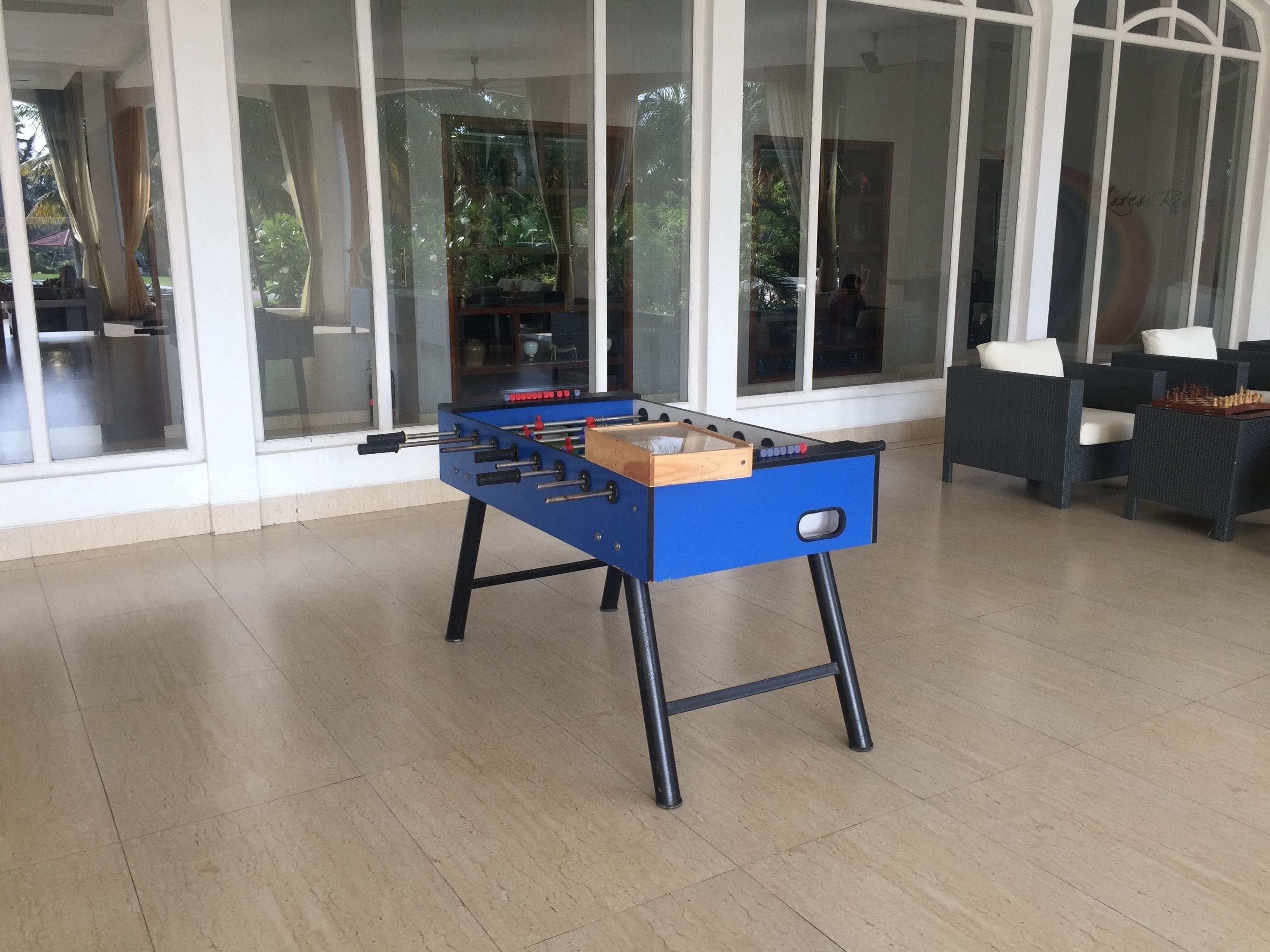 A foosball table in a room with large windows, a ceiling fan, and a seating area with a table and chairs.