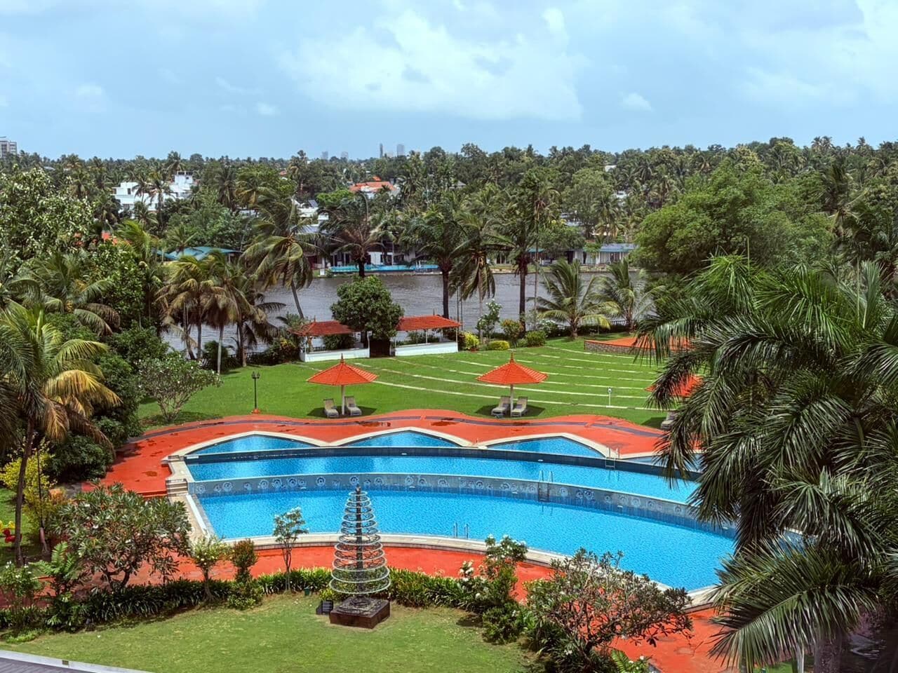 A swimming pool with a red deck, surrounded by palm trees and a grassy area with lounge chairs.