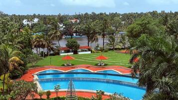 A swimming pool with a red deck, surrounded by palm trees and a grassy area with lounge chairs.