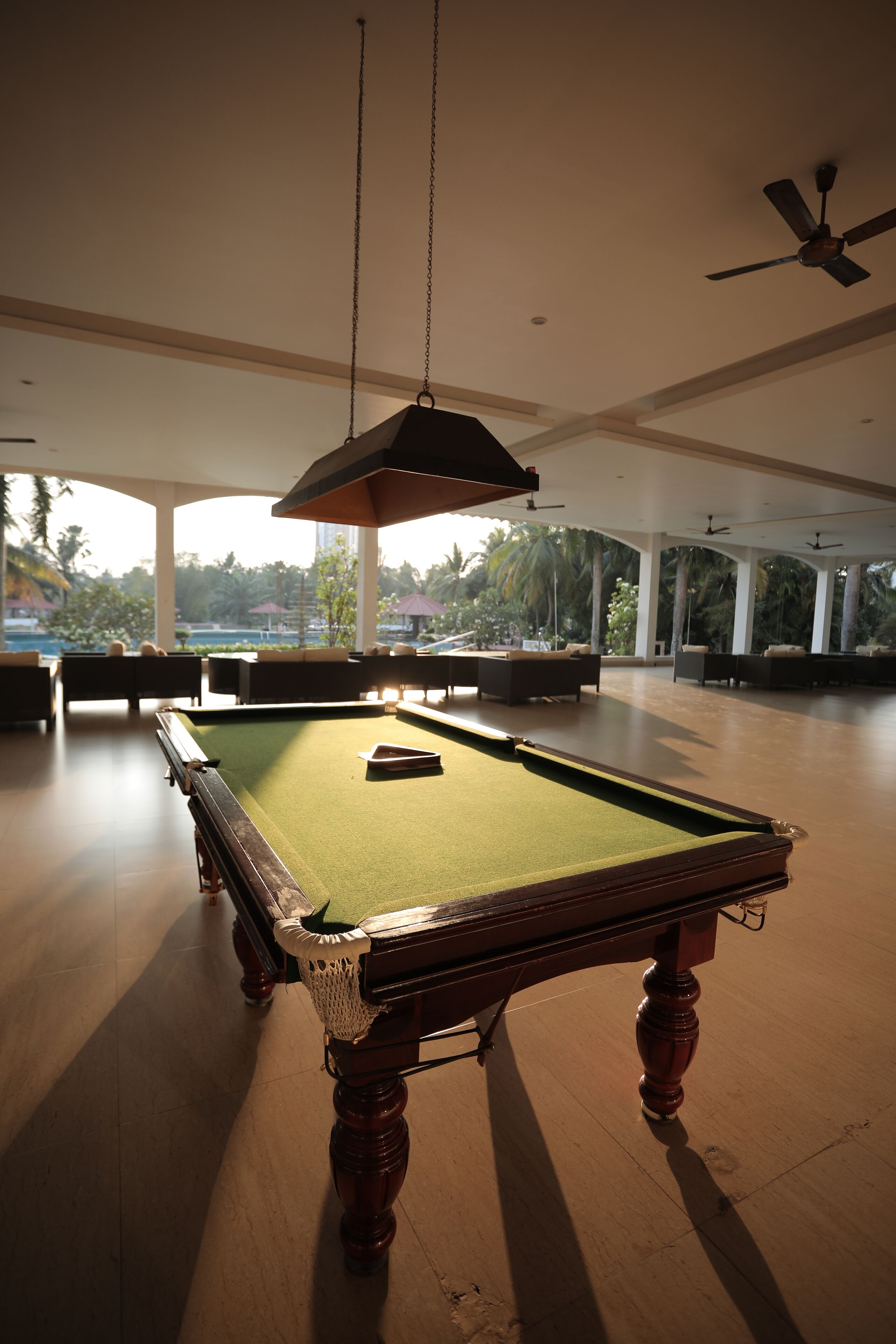 A pool table in a spacious room with ceiling fans and large windows offering a view of palm trees.