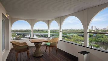 Un balcón con una mesa de madera y sillas de mimbre, con vistas a un paisaje urbano y un río.