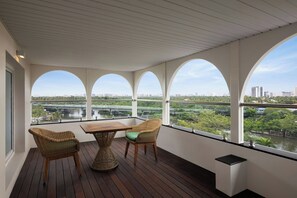 Un balcón con una mesa de madera y sillas de mimbre, con vistas a un paisaje urbano y un río.