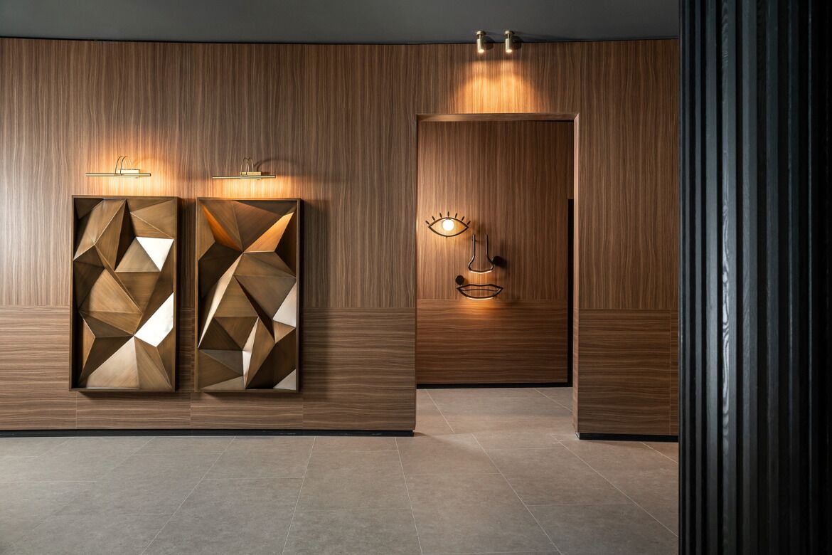 A hallway with wooden paneling, geometric wall art, and wall-mounted lighting fixtures.