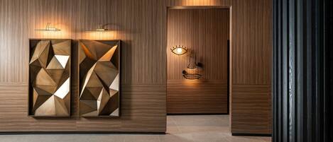 A hallway with wooden paneling, geometric wall art, and wall-mounted lighting fixtures.
