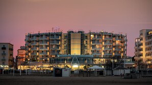 A multi-story hotel with balconies, a swimming pool, and a beach area.