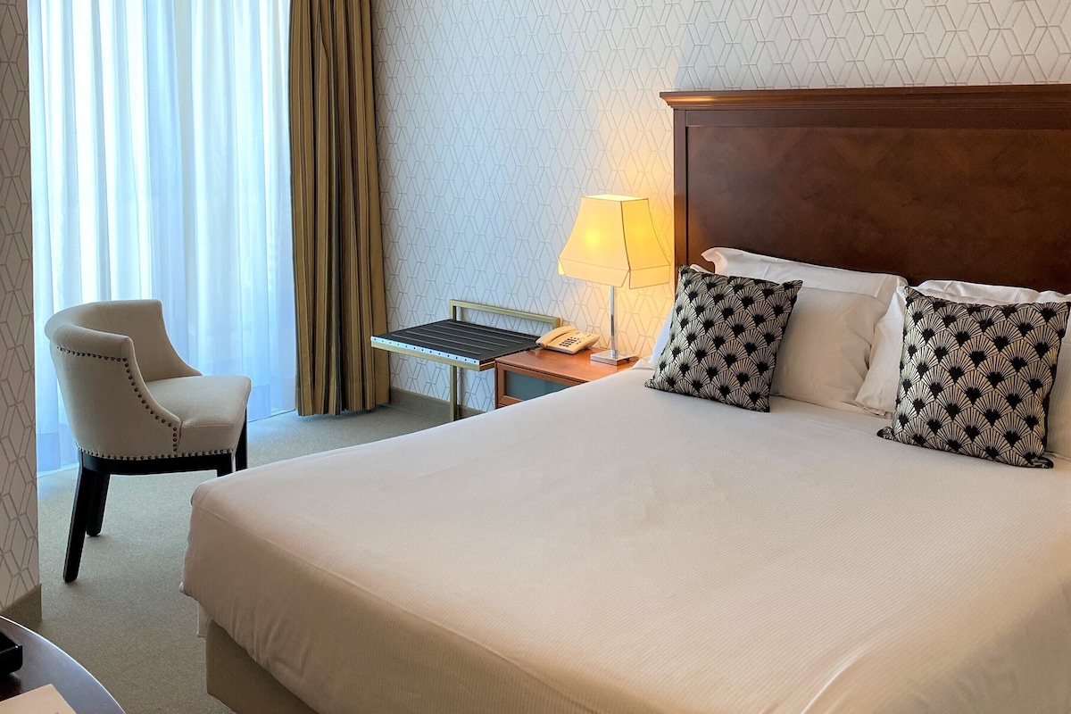 Een hotelkamer met een groot bed, een stoel, een bureau met een lamp en een kamerwand met een patroon.