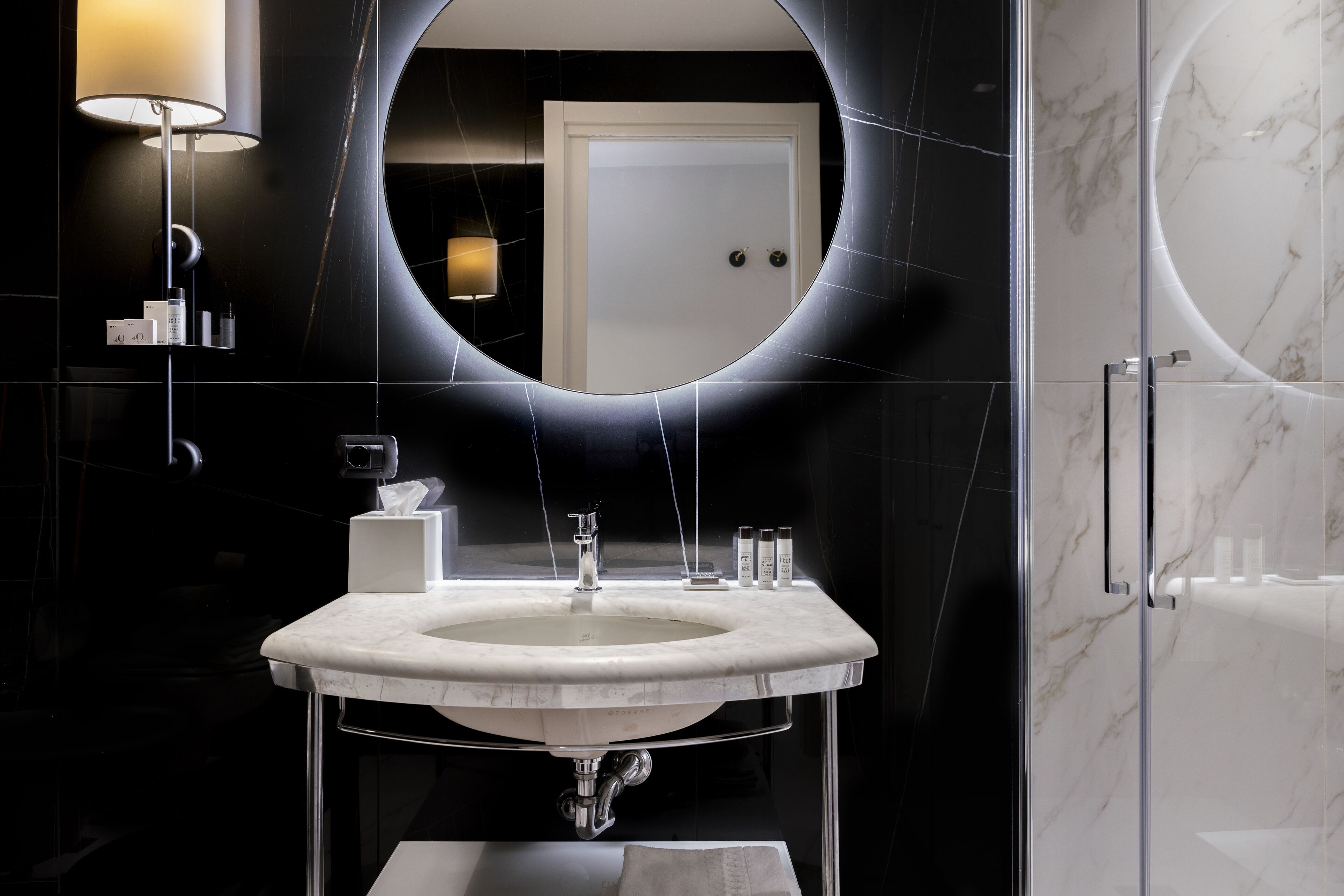 Une salle de bain moderne avec un grand miroir ovale, un lavabo blanc et une cabine de douche en verre.