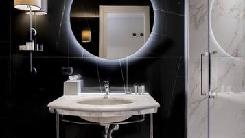 Une salle de bain moderne avec un grand miroir ovale, un lavabo blanc et une cabine de douche en verre.