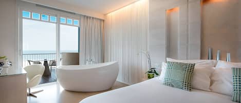 Una habitación de hotel moderna con una cama grande, una bañera, un escritorio y un balcón con vistas.