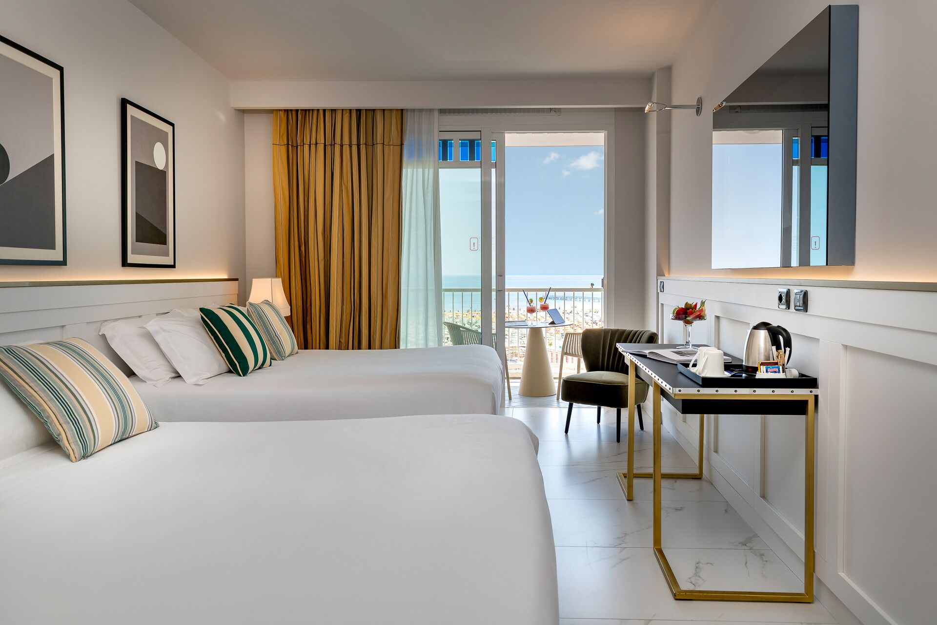 Ein Hotelzimmer mit zwei Betten, einem Schreibtisch, einem Stuhl, einem Balkon mit Aussicht und einem großen Spiegel.