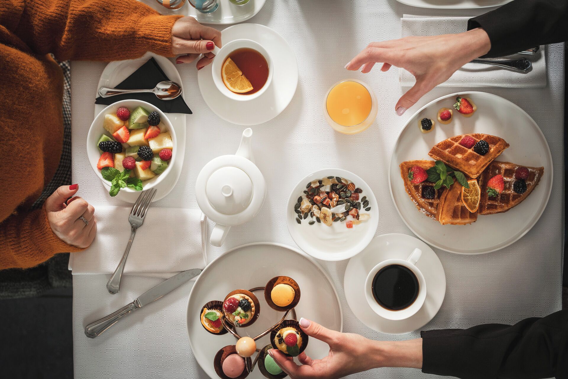 Un desayuno con diversos platos, como waffles, ensalada de frutas y pasteles.