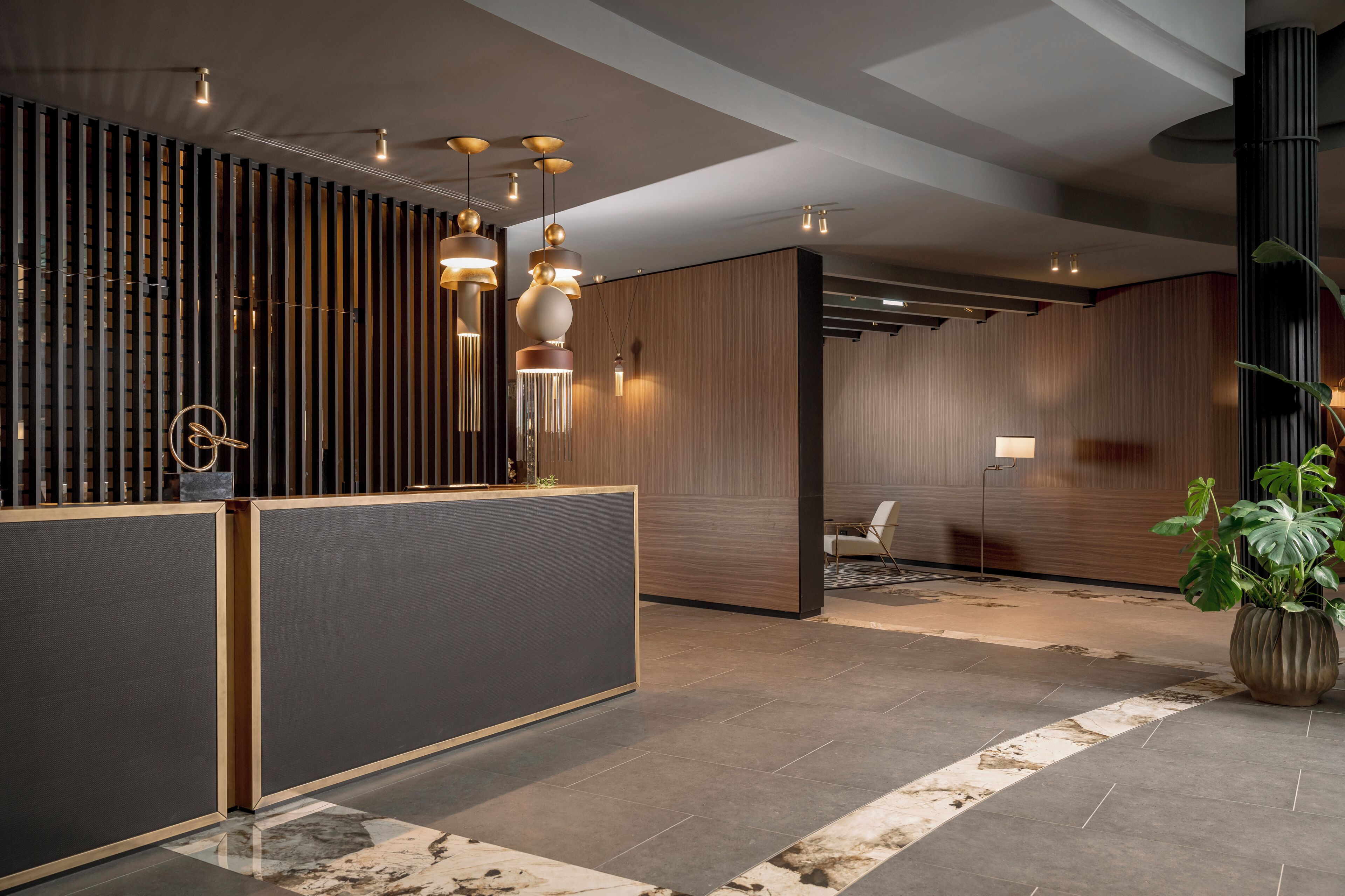 A reception area with a modern design, featuring a reception desk, vertical wooden slats, and pendant lighting.