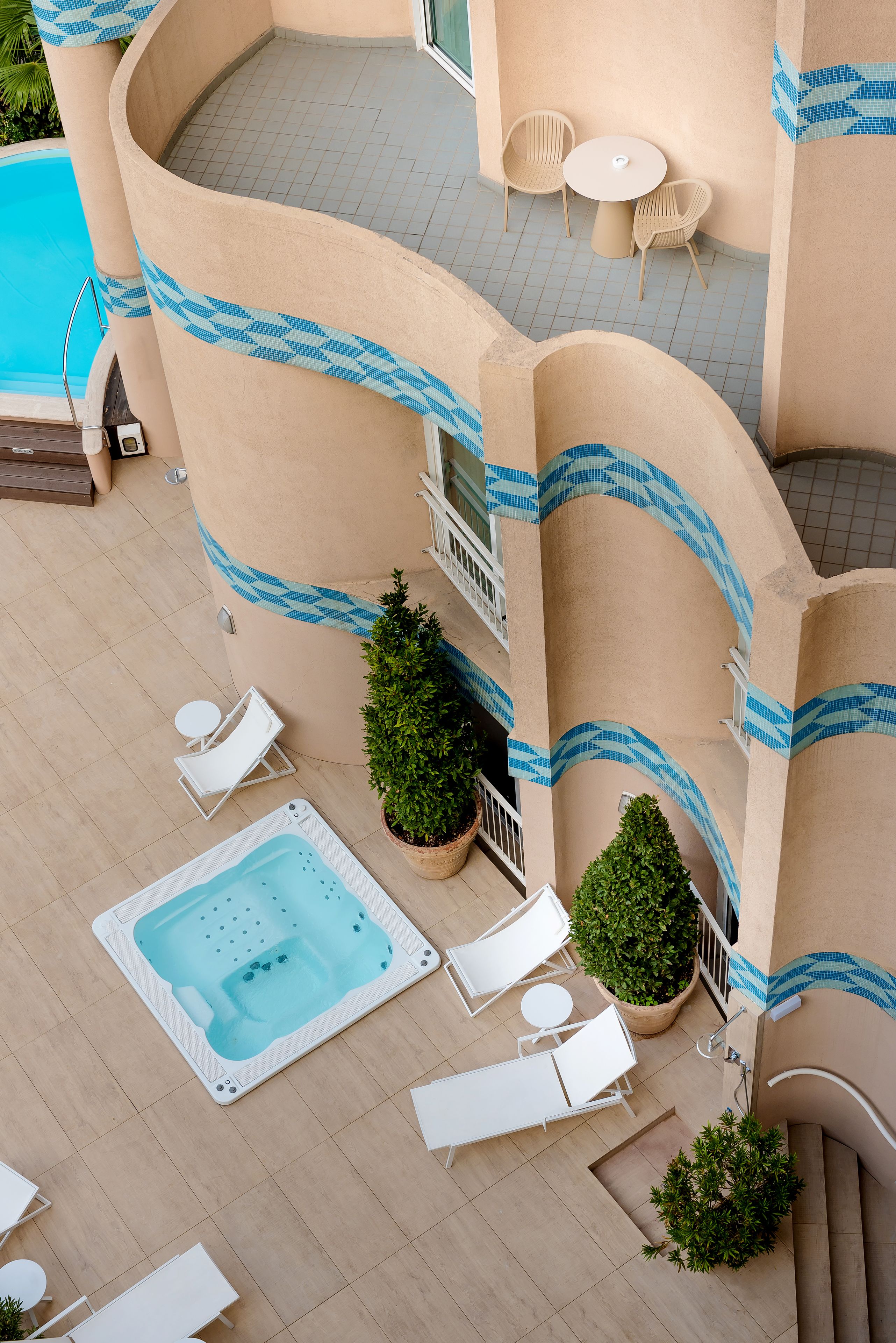 Un área de piscina en la azotea con sillones de descanso, un jacuzzi y plantas en macetas.