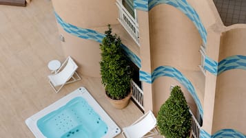 Un área de piscina en la azotea con sillones de descanso, un jacuzzi y plantas en macetas.