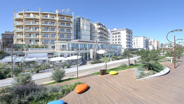 A modern hotel with multiple balconies, a covered outdoor area, and a wooden deck with seating.