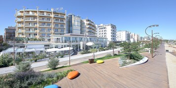 Un hotel moderno con numerosi balconi, una zona esterna coperta e un pontile in legno con posti a sedere.