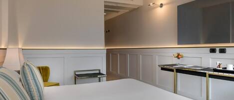 A modern hotel room with a large bed, a small desk, and a kitchenette.