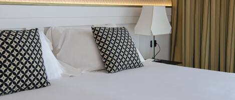Habitación de hotel con una cama bien tendida, almohadas con estampado geométrico, una lámpara de noche y un techo con textura.