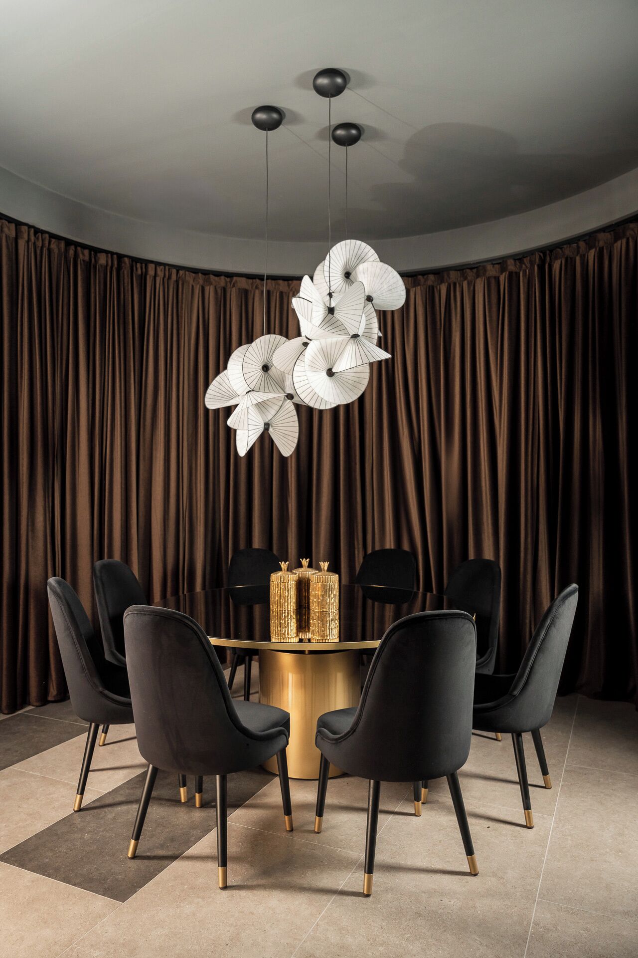 A dining area with a round table, black chairs, a gold bar, and a curtain backdrop.