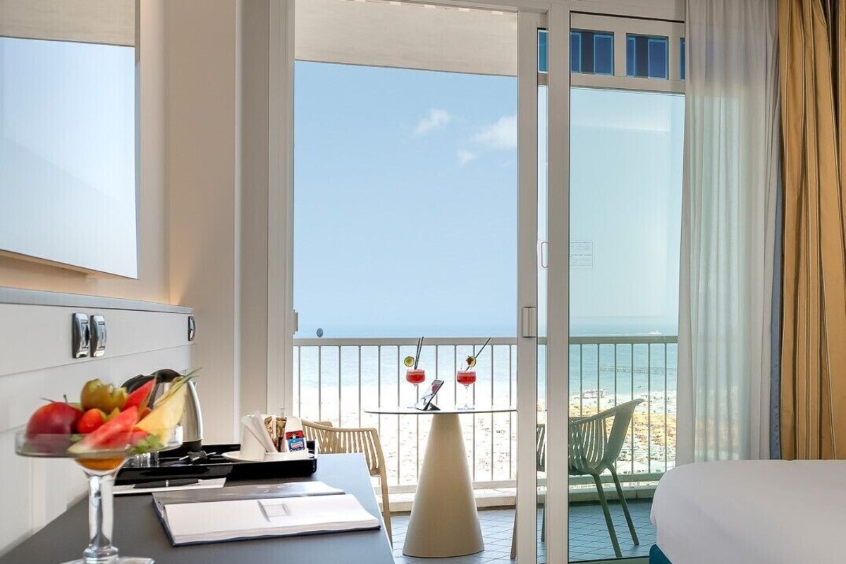 Een hotelkamer met balkon, een eettafel met een fruitschaal en een bed.