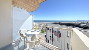 A balcony with a white table and chairs, a wooden ceiling, and a view of the sea and cityscape.
