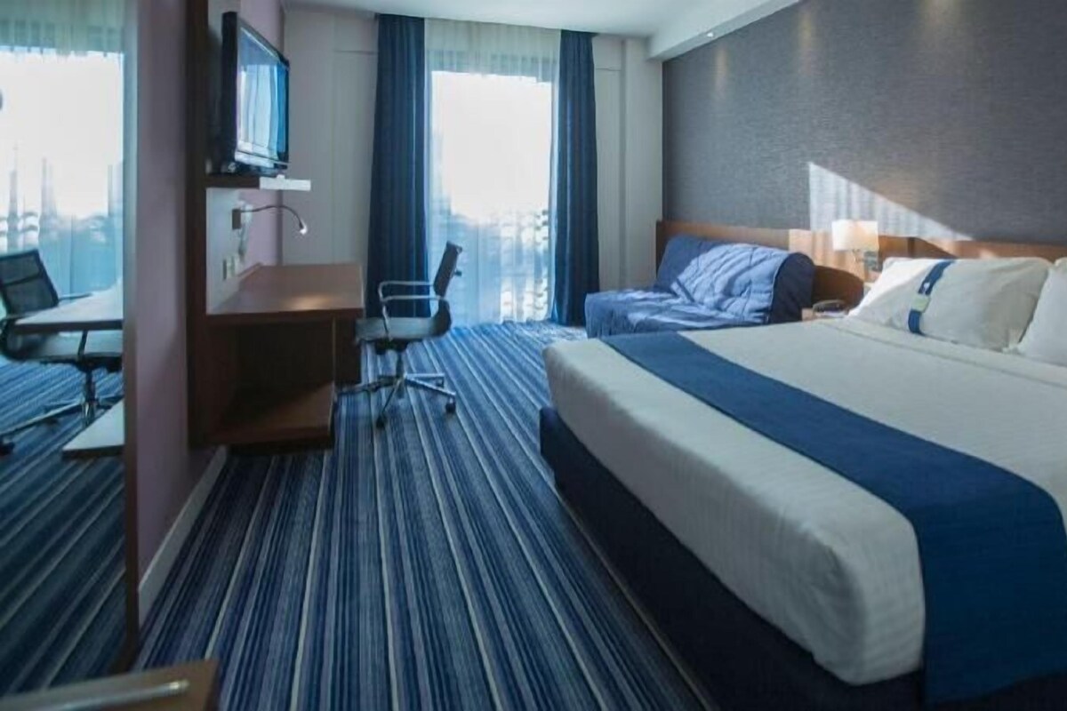 A hotel room with a large bed, a desk, a chair, and a TV.