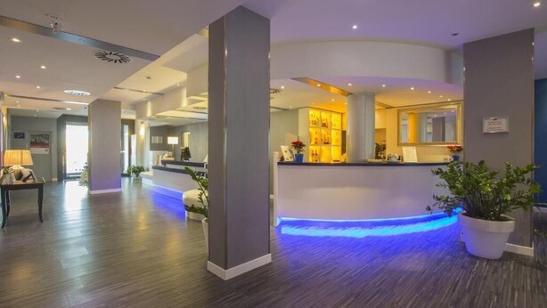 Un hall d’hôtel moderne avec un comptoir d’accueil, un espace de réception éclairé de lumière bleue et un plancher en bois.