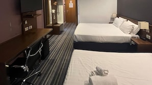 Une chambre d’hôtel avec un grand lit, un lit plus petit, une télévision, un bureau avec une chaise et un miroir.