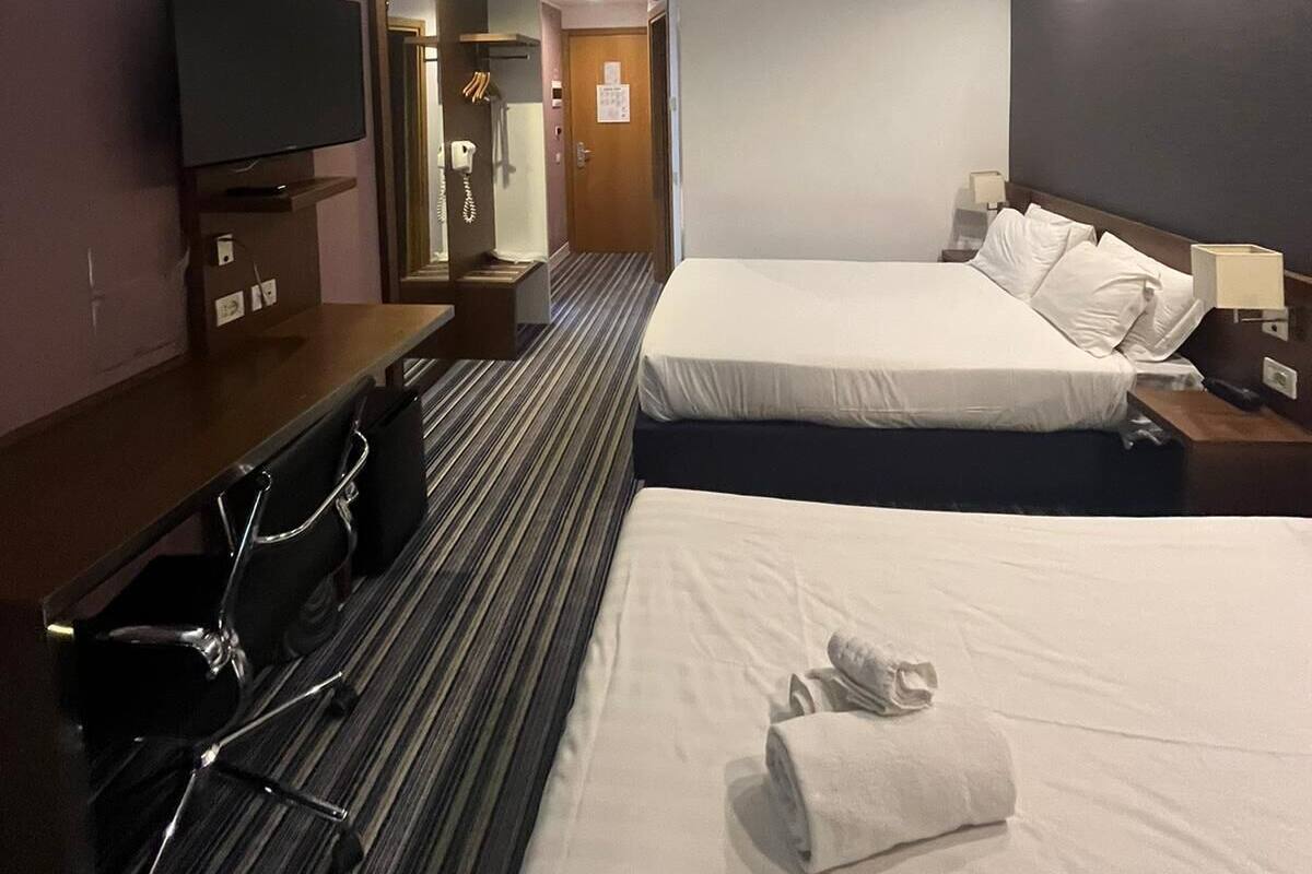 A hotel room with a large bed, a smaller bed, a TV, a desk with a chair, and a mirror.
