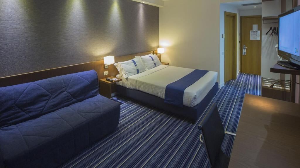 A hotel room with a bed, a sofa, a TV, and a desk.