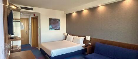 Ein Hotelzimmer mit Bett, Schreibtisch, Stuhl, Sofa und Fernseher.
