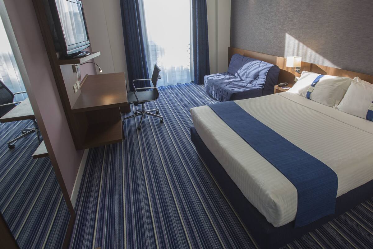 A hotel room with a large bed, a desk, and a chair.