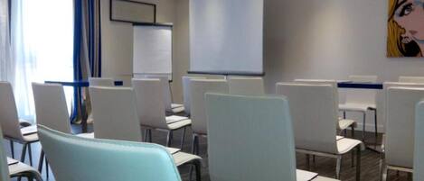 A conference room with rows of white chairs, a projector screen, and a whiteboard.