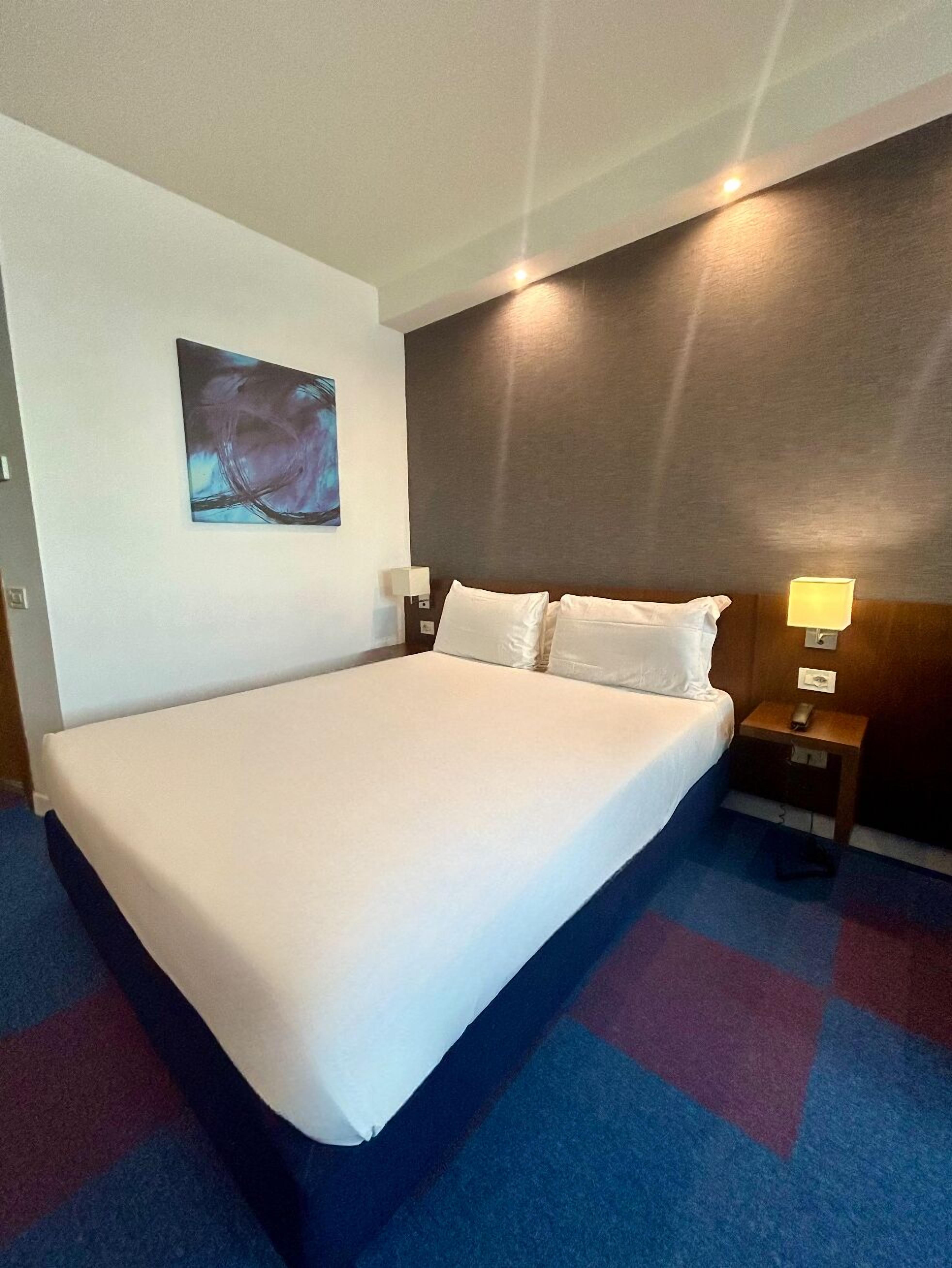 Une chambre d’hôtel avec un grand lit, une table de chevet avec une lampe et un tableau au mur.