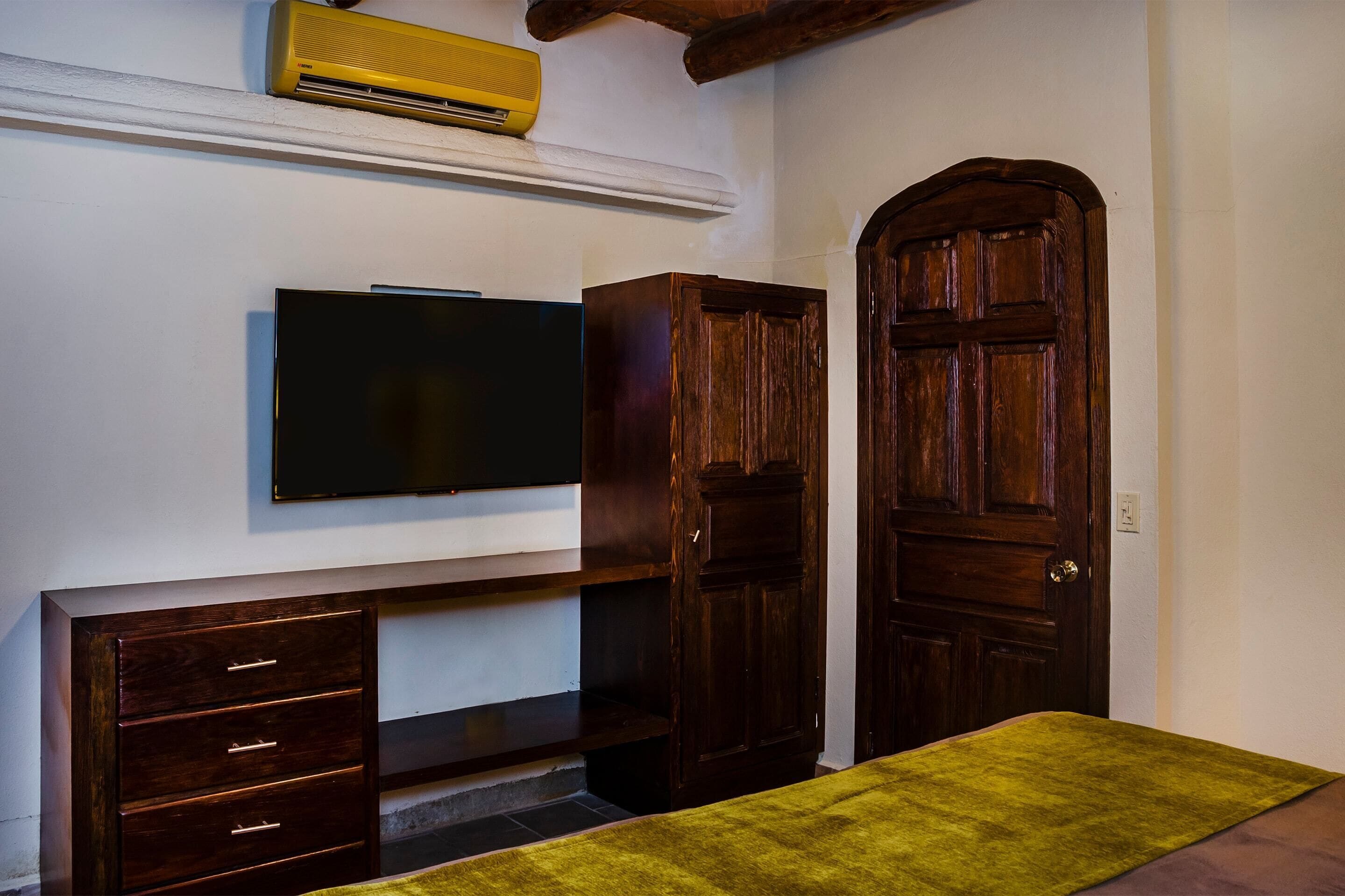 A room with a wooden wardrobe, a television mounted on the wall, and a green rug on the floor.
