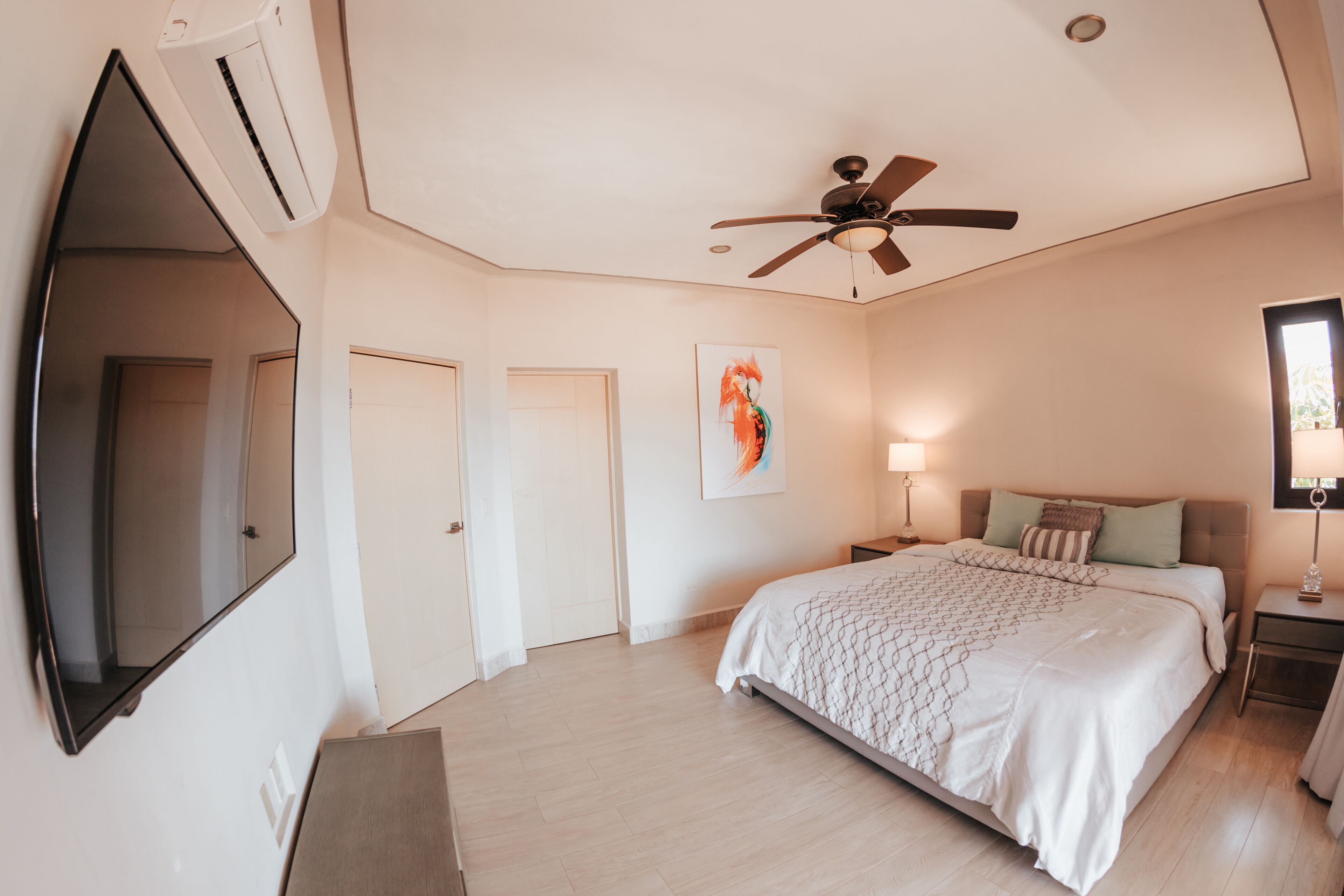 A bedroom with a bed, a ceiling fan, a TV, and a painting on the wall.