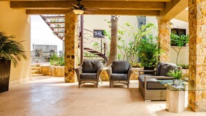 A covered outdoor seating area with wicker furniture and a glass table, surrounded by stone pillars and potted plants. - Castillo Blarney Inn (Cabo San Lucas)