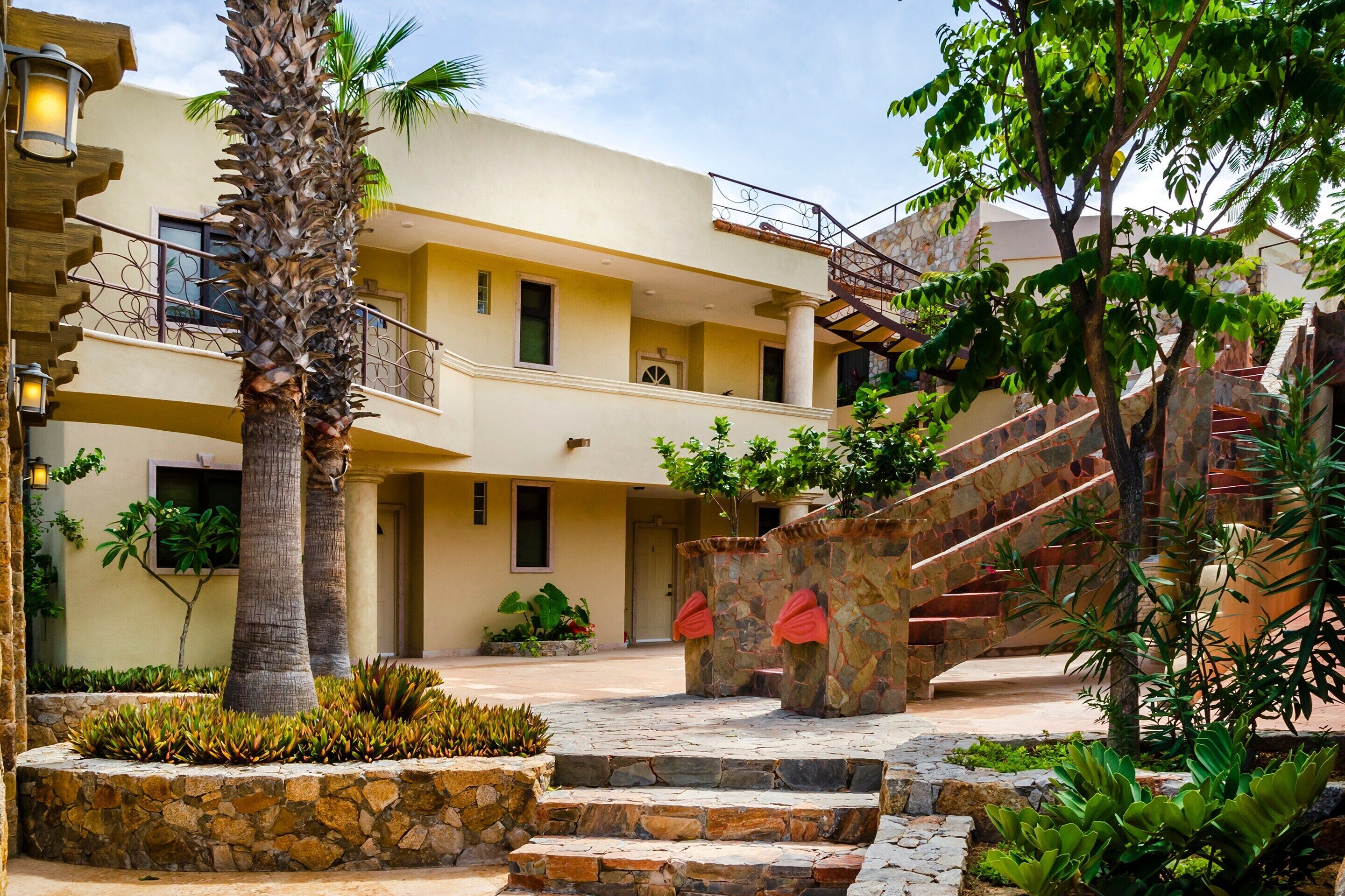 Un edificio de varios pisos con una escalera de piedra, palmeras y un jardín bien cuidado.