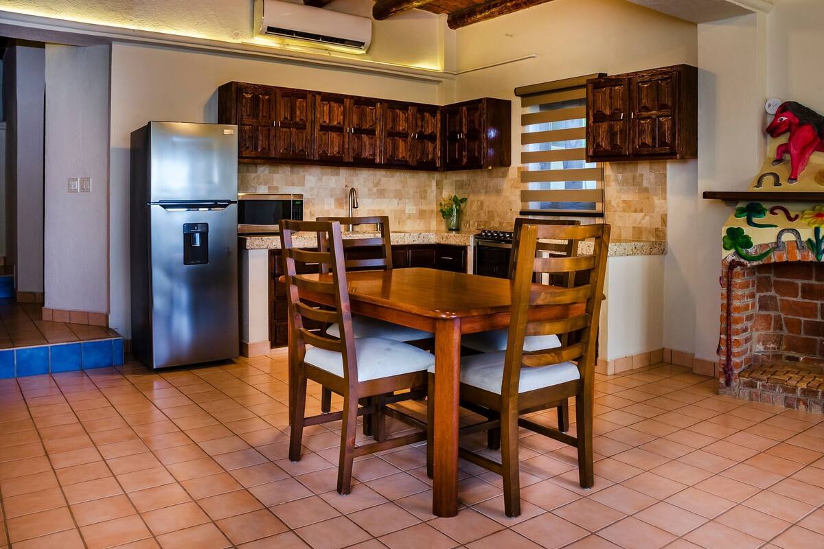 Una cocina con armarios de madera, un refrigerador de acero inoxidable, una mesa de comedor con sillas y una chimenea de ladrillo.