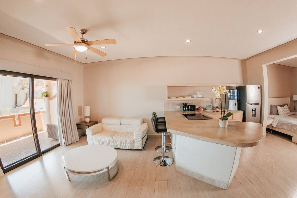 Una habitación de hotel moderna con cocina, una mesa de comedor, un sofá y un ventilador de techo.