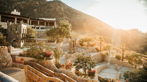 A courtyard with stone steps, potted plants, and a building with multiple windows and balconies. - Castillo Blarney Inn (Cabo San Lucas)
