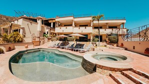 A pool area with lounge chairs, a hot tub, and a building with multiple balconies. - Castillo Blarney Inn (Cabo San Lucas)