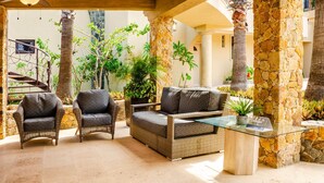 A cozy outdoor seating area with wicker furniture and a glass table, surrounded by stone pillars and lush greenery. - Castillo Blarney Inn (Cabo San Lucas)