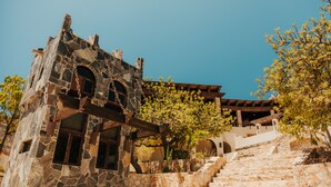 A stone building with arched windows and a staircase leading up to a wooden deck. - Castillo Blarney Inn (Cabo San Lucas)