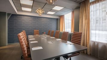 A conference room with a long table, brown upholstered chairs, a patterned wall, and a large window with curtains.