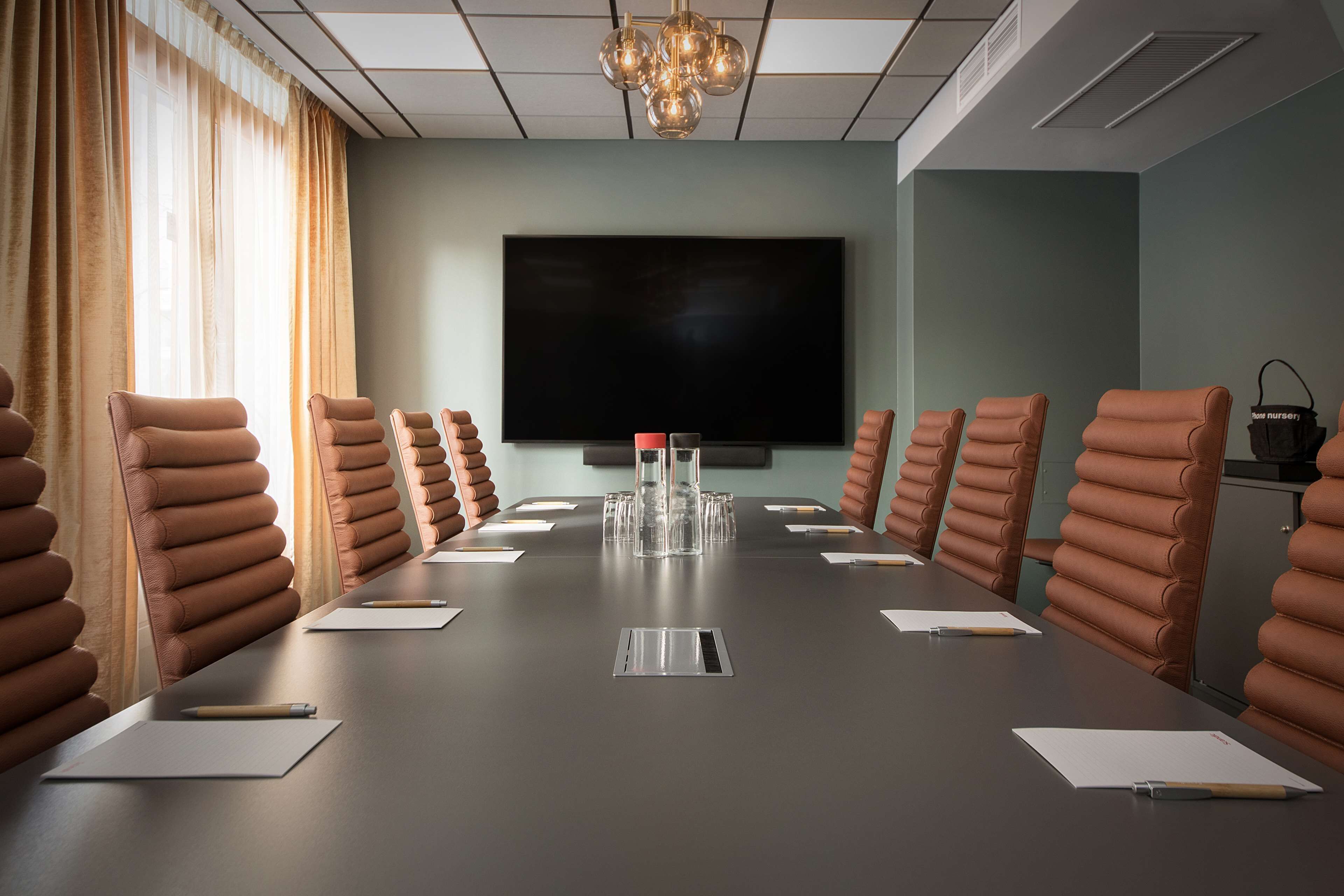 A conference room with a long table, brown chairs, a large screen, and a chandelier.