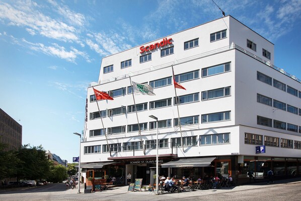 Un edificio blanco con el nombre "Scandic" en la parte superior. Hay banderas en el edificio y un letrero que dice "Scandic St. Olav's Passage".