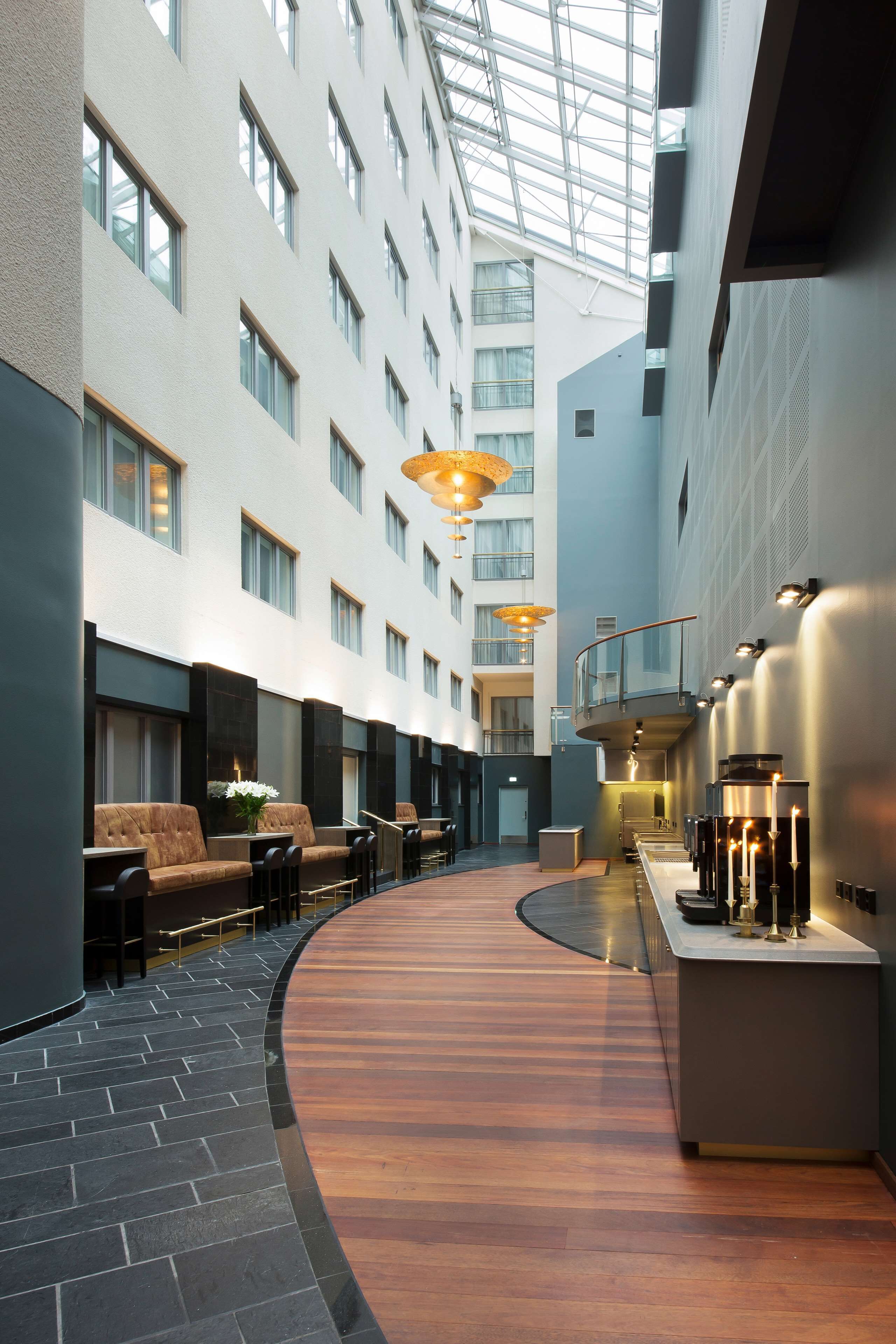 A modern hotel lobby with a curved wooden floor, seating areas, and a glass ceiling.