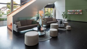 A modern lobby with a staircase, sofas, ottomans, a coffee table, and a bookshelf.