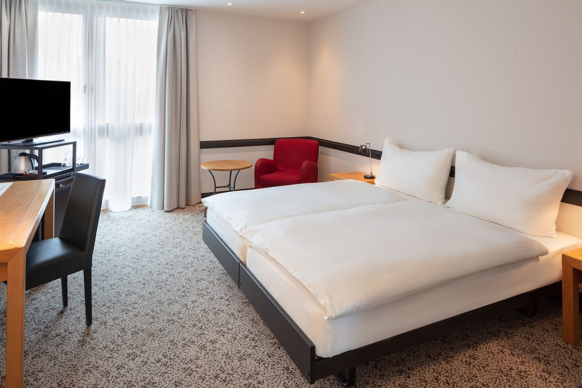 Una habitación de hotel con una cama, un escritorio con silla, un televisor y una mesita.